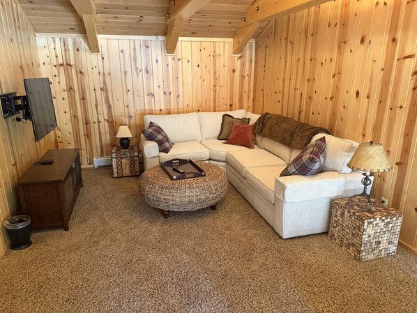 Una habitación acogedora con sofá, reposapiés y una mesita de noche con lámpara.