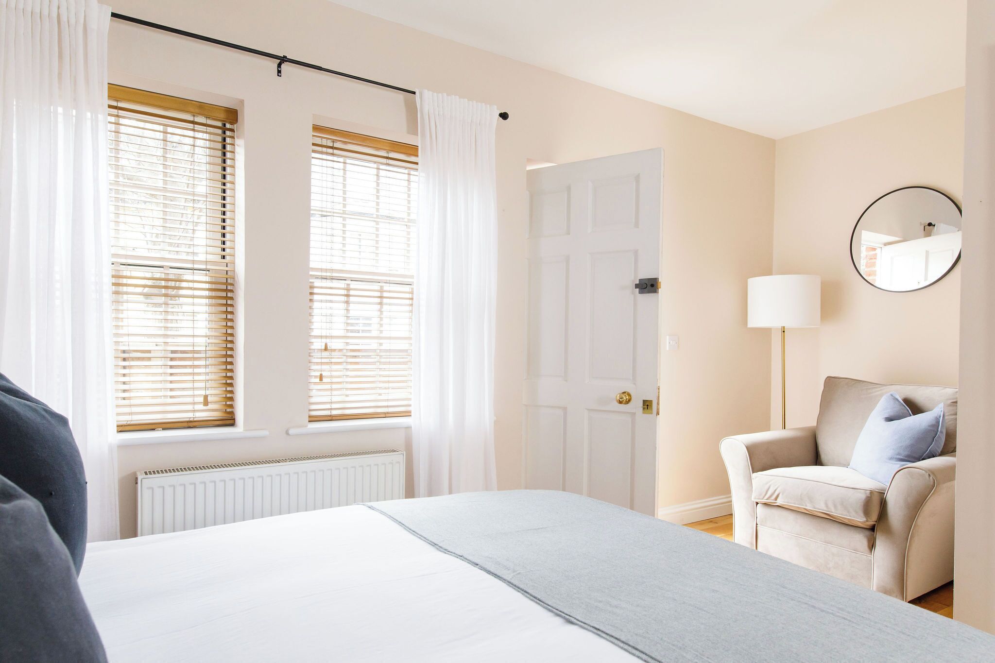 Ein Hotelzimmer mit Bett, Sessel, Lampe und Tür.