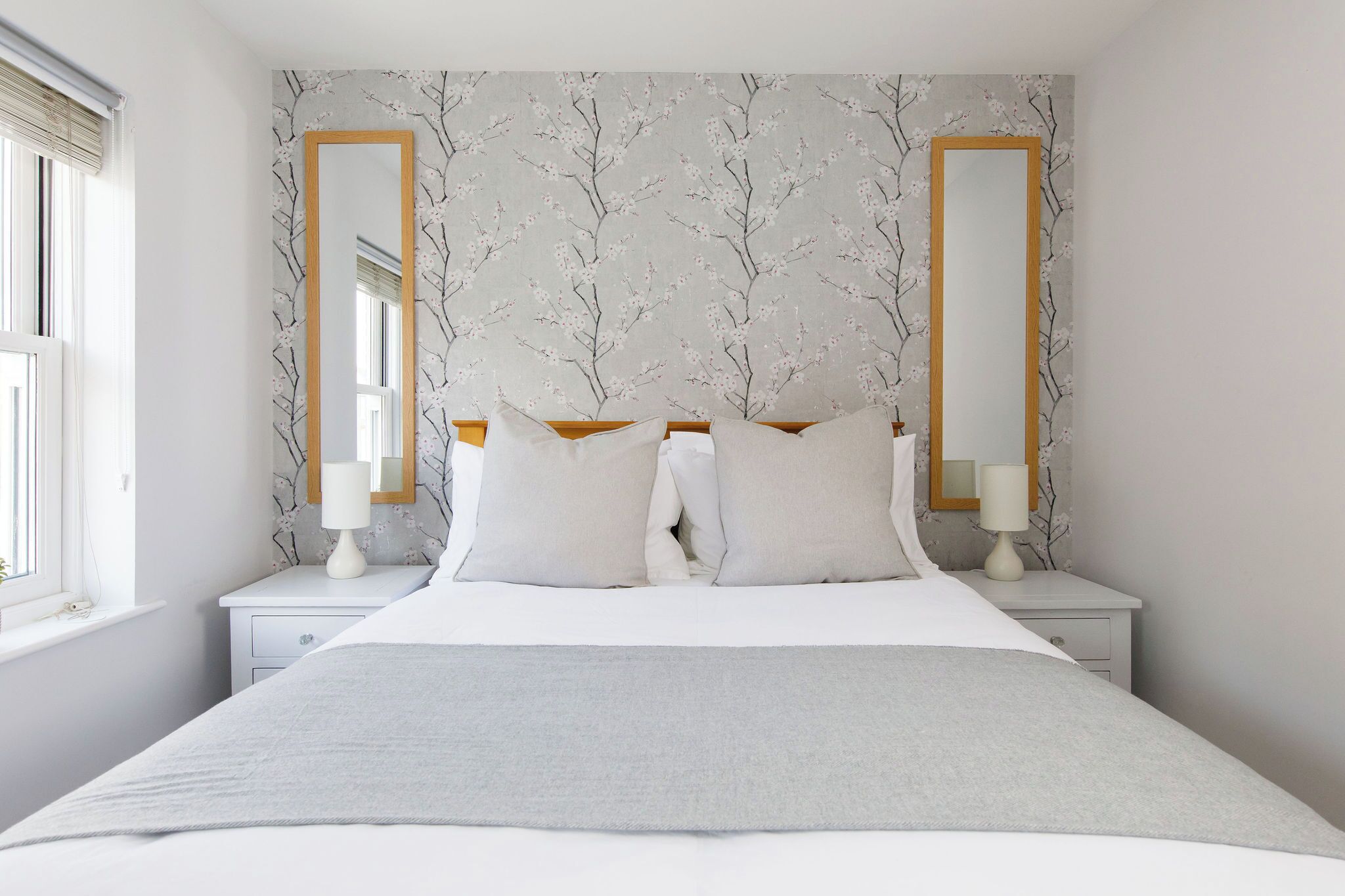 Een slaapkamer met een groot bed, twee nachtkastjes, twee spiegels aan de muur, en een raam met zonwering.