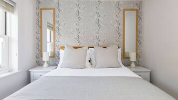 Een slaapkamer met een groot bed, twee nachtkastjes, twee spiegels aan de muur, en een raam met zonwering.