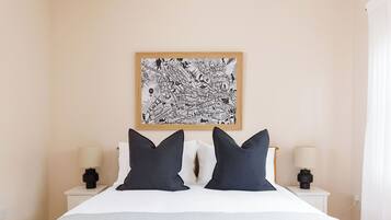 Een net opgemaakt bed met twee kussens, een abstract kunstwerk aan de muur en twee nachtkastjes met lampen.