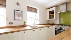 Een keuken met witte kastjes, een houten aanrecht, een spoelbak, een fornuis en een raam met uitzicht op gebouwen.
