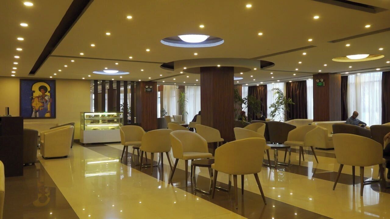 Een hotel lobby met een gepolijste vloer, meerdere zithoeken, een receptiebalie en een groot raam met gordijnen.