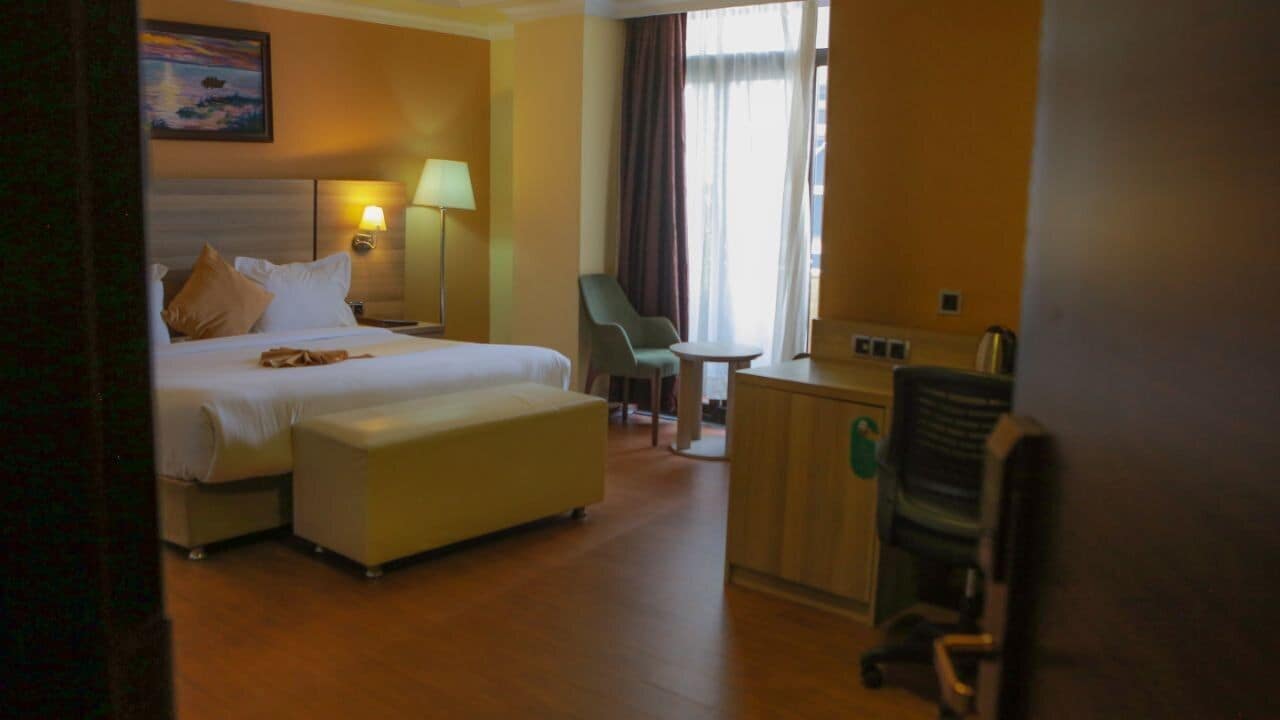 Quarto de hotel com cama, escrivaninha, cadeira e mesa pequena.