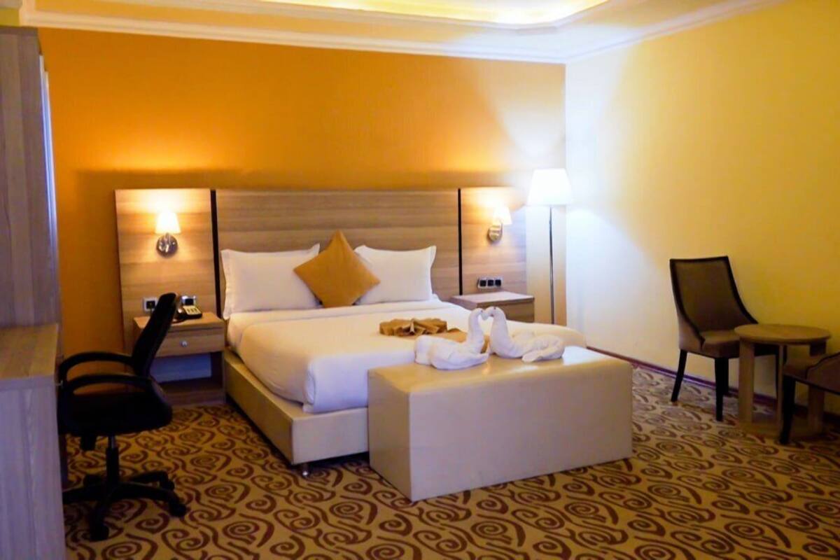 A hotel room with a large bed, two bedside tables, a desk with a chair, and a small table with two chairs.