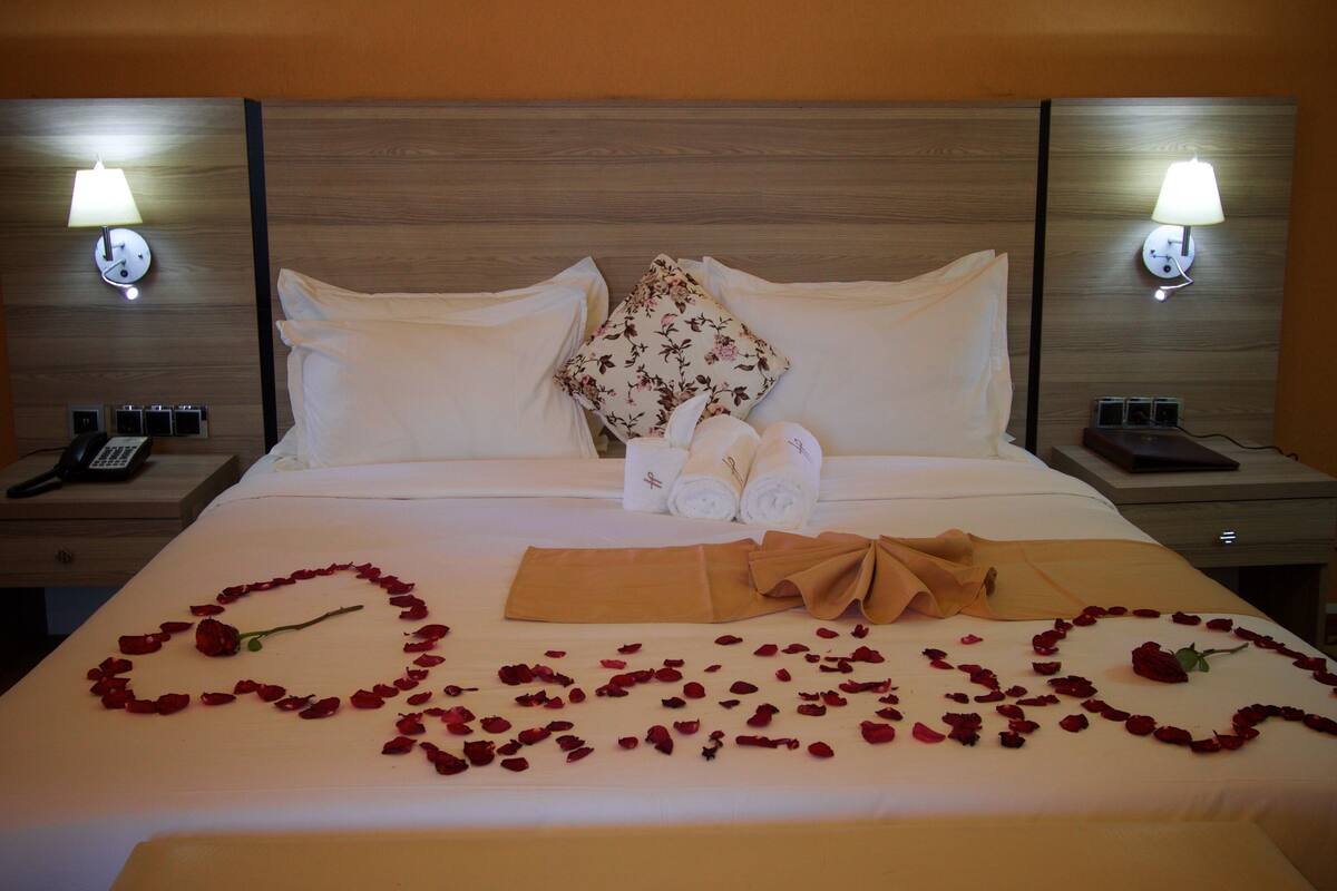 A hotel room with a neatly made bed, two bedside lamps, a telephone, and a laptop on a nightstand.