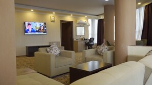 Ein Hotelzimmer mit Wohnbereich, ausgestattet mit zwei Sofas, einem Couchtisch, einem an der Wand befestigten Fernseher und einer kleinen Küchenzeile.
