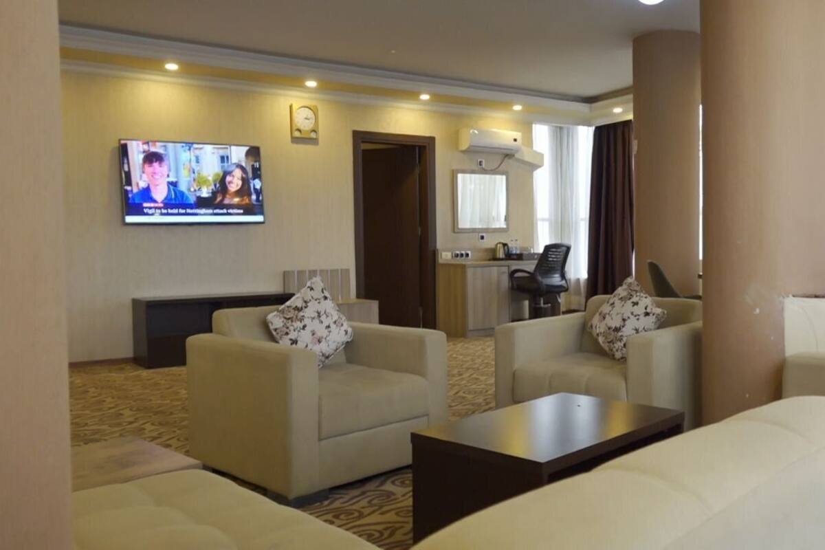 A hotel room with a living area featuring two sofas, a coffee table, a TV mounted on the wall, and a small kitchenette.
