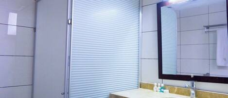 A bathroom with a large mirror, a sink with toiletries, and a shower enclosure.