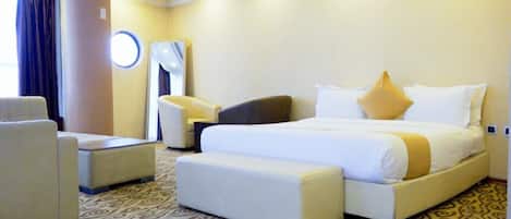 A hotel room with a large bed, a sofa, a chair, and a round mirror.