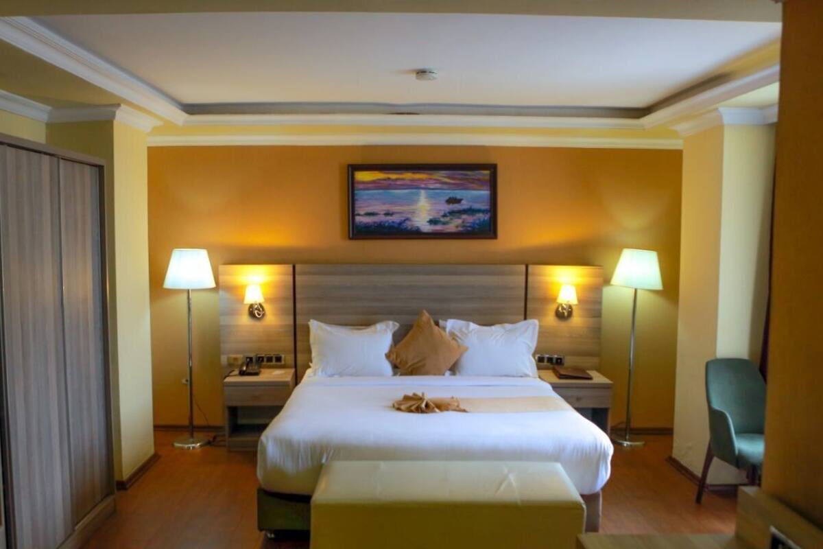 A hotel room with a large bed, two bedside lamps, a painting on the wall, and a chair.