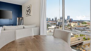 A modern living room with a large window, a flat-screen TV, a sofa, and a dining table. - The Malibu Suite Penthouse The Gulch
 (Nashville)