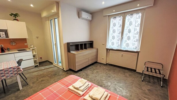 A compact bedroom with a bed, a small desk, a chair, a radiator, and a window with curtains. - Apartment Giallo by Interhome (Rapallo)