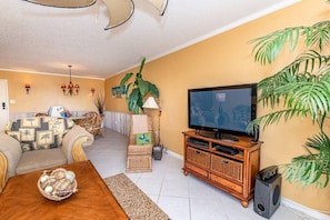A living room with a sofa, a coffee table, a TV, and a speaker. - Parrot Party - Ocean House 319 (St. Augustine)