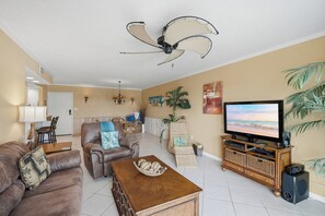 A living room with a sofa, armchair, coffee table, television, and a ceiling fan. - Parrot Party - Ocean House 319 (St. Augustine)