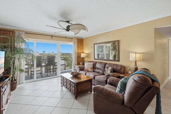 A living room with a sofa, coffee table, and a ceiling fan. - Parrot Party - Ocean House 319 (St. Augustine)