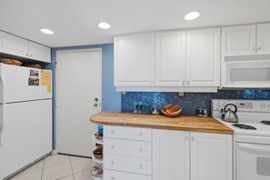 A kitchen with white cabinets, a wooden countertop, a microwave, and a stove. - Parrot Party - Ocean House 319 (St. Augustine)
