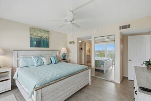 A bedroom with a bed, a ceiling fan, a nightstand, a lamp, a painting, and a door leading to a balcony. - Parrot Party - Ocean House 319 (St. Augustine)