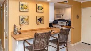 Una cocina con una isla de madera, dos sillas de mimbre y cuatro cuadros colgados en la pared.