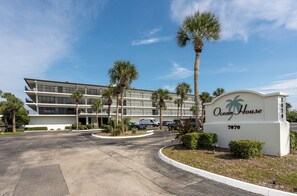A multi-story hotel with a sign reading 'Ocean House 7870' and a parking lot with several cars. - Parrot Party - Ocean House 319 (St. Augustine)