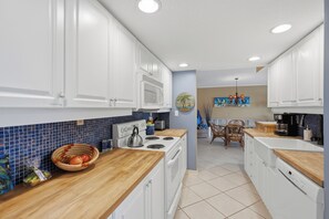 A kitchen with white cabinets, a wooden countertop, a stove, and a microwave. - Parrot Party - Ocean House 319 (St. Augustine)