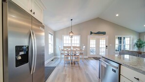 A spacious kitchen with a stainless steel refrigerator, a dining area with a wooden table and chairs, and a kitchen island with a built-in dishwasher.