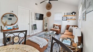 Un salon avec un canapé marron, une table basse en verre, un ventilateur de plafond et un téléviseur.