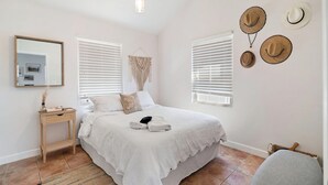 Une chambre à coucher avec un lit, une table de chevet, des chapeaux accrochés au mur et une décoration en macramé suspendue.