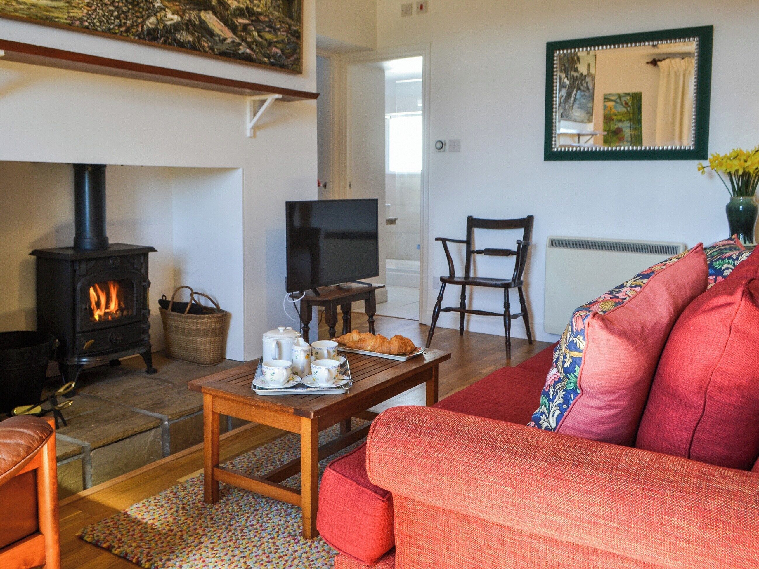 A cozy living room with a fireplace, a television, a dining table with cups and a croissant, and a red sofa.