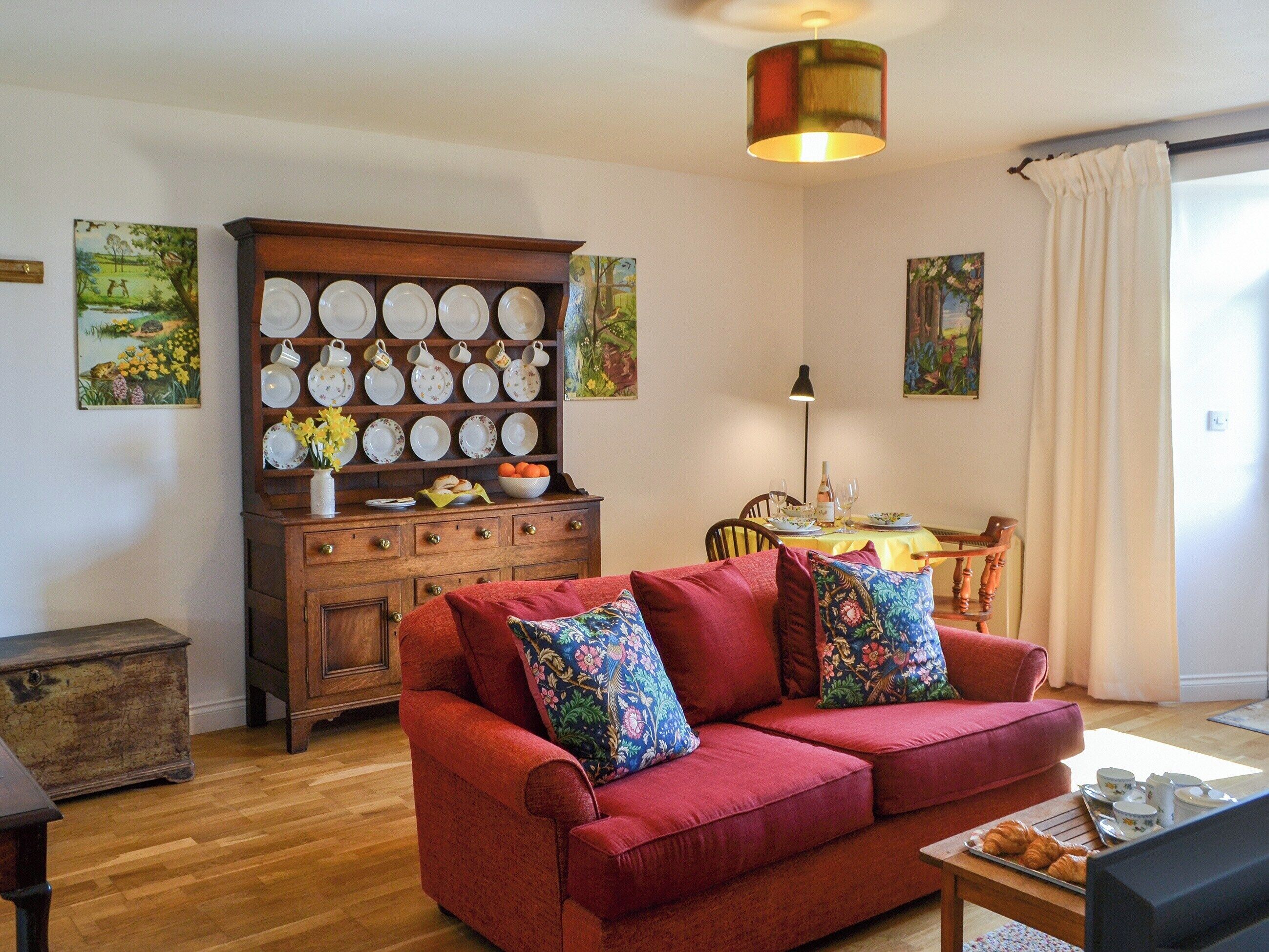 A cozy living room with a red sofa, wooden cabinet with dishes, and paintings on the walls.