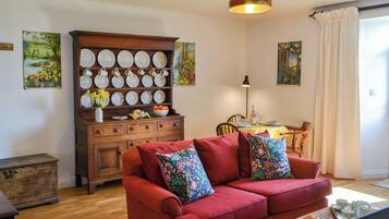 A cozy living room with a red sofa, wooden cabinet with dishes, and paintings on the walls.