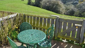 Een groene metalen tafel en stoelen in een tuin met een houten omheining en een poort.