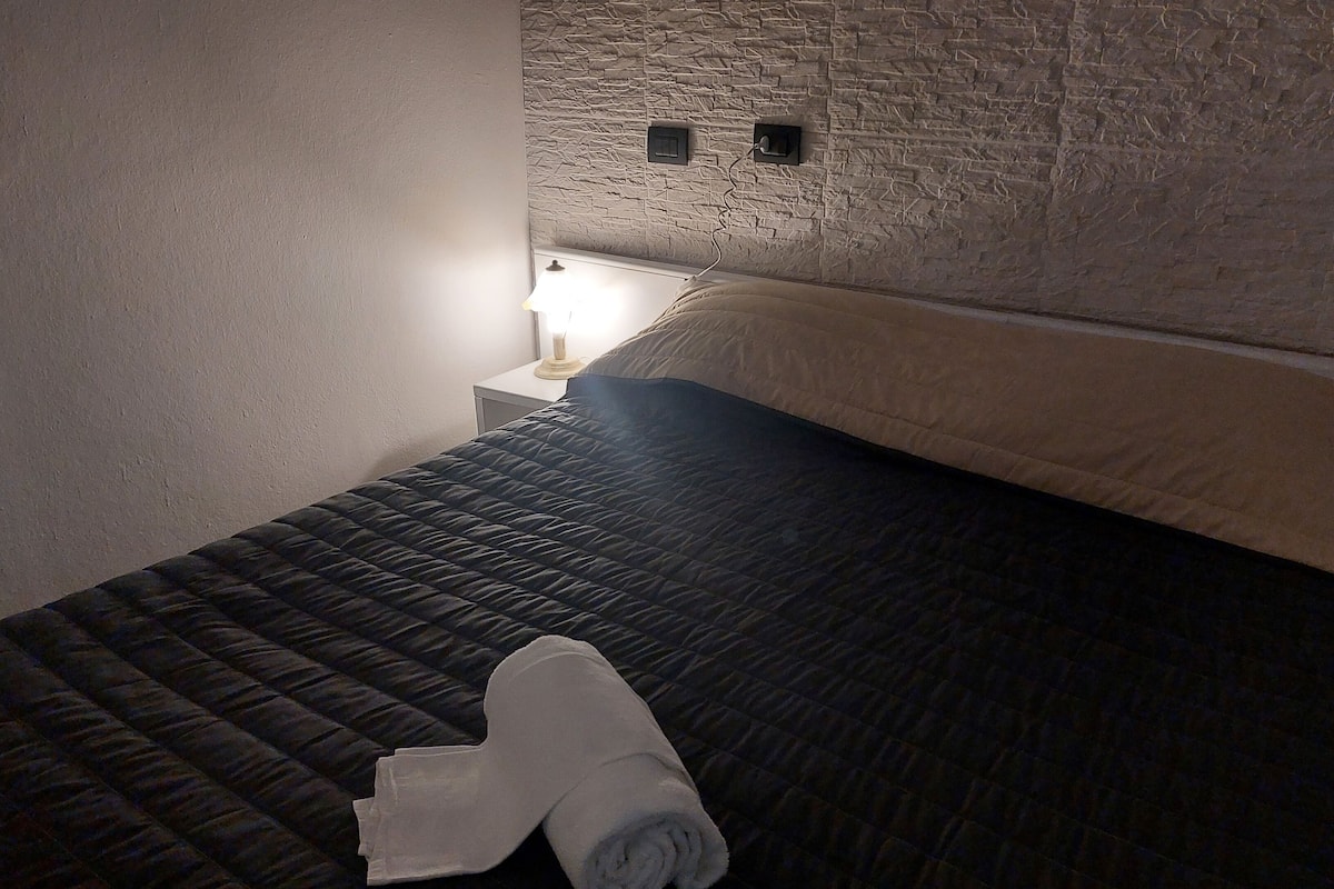 Une petite pièce agréable et confortable, avec un lit, une table de chevet et une lampe fixée au mur.