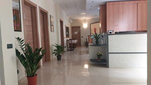 Un pasillo con puertas de madera, una recepción, un área de comedor y plantas en macetas.