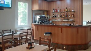 Una zona de bar con una máquina de café, estantes con botellas de licor y un área de estar con mesas y sillas.