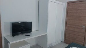 Una habitación con una televisión sobre un mueble blanco, un armario y una puerta de madera.