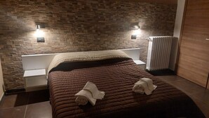 Un dormitorio moderno con cabecera estampada en piedra, una cama bien hecha con colcha marrón y dos lámparas de pared.