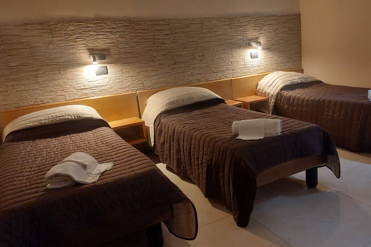 Une chambre d’hôtel avec trois lits simples, chacun doté d’une tête de lit en bois et d’une table de chevet.