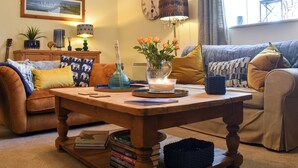 Een gezellige woonkamer met een houten salontafel, een klok, een lamp, een stadsgezicht in een lijst en een bank met kussens.
