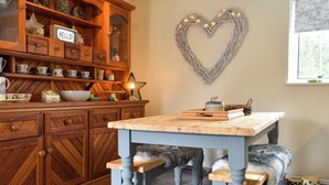 Een keuken met houten keukenkastjes, een hartvormige decoratie aan de muur en een tafel met bankjes.