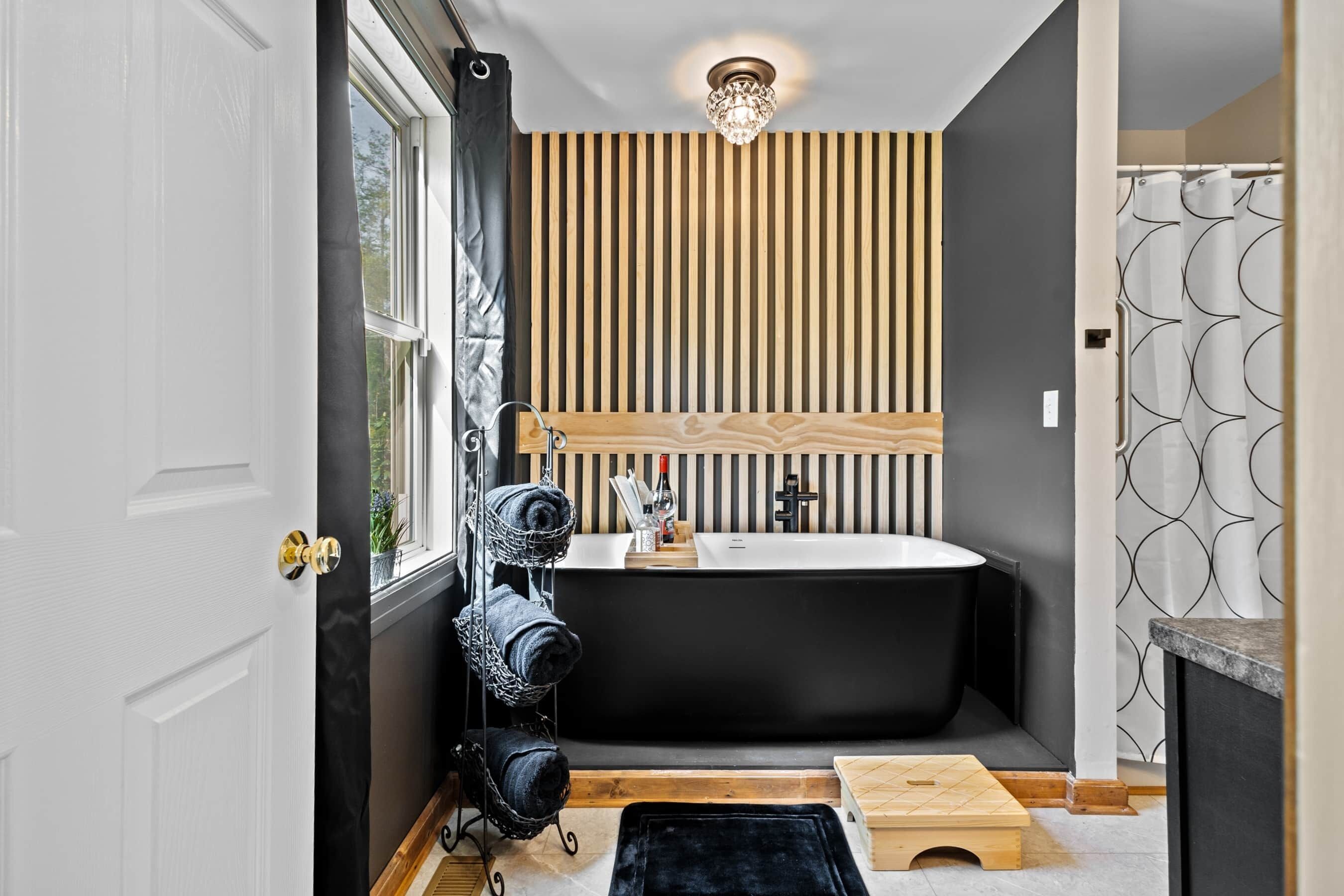 Un baño moderno con una bañera independiente, un revestimiento de pared de listones de madera y una cortina de ducha negra.