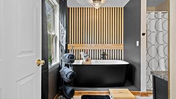 Un baño moderno con una bañera independiente, un revestimiento de pared de listones de madera y una cortina de ducha negra.