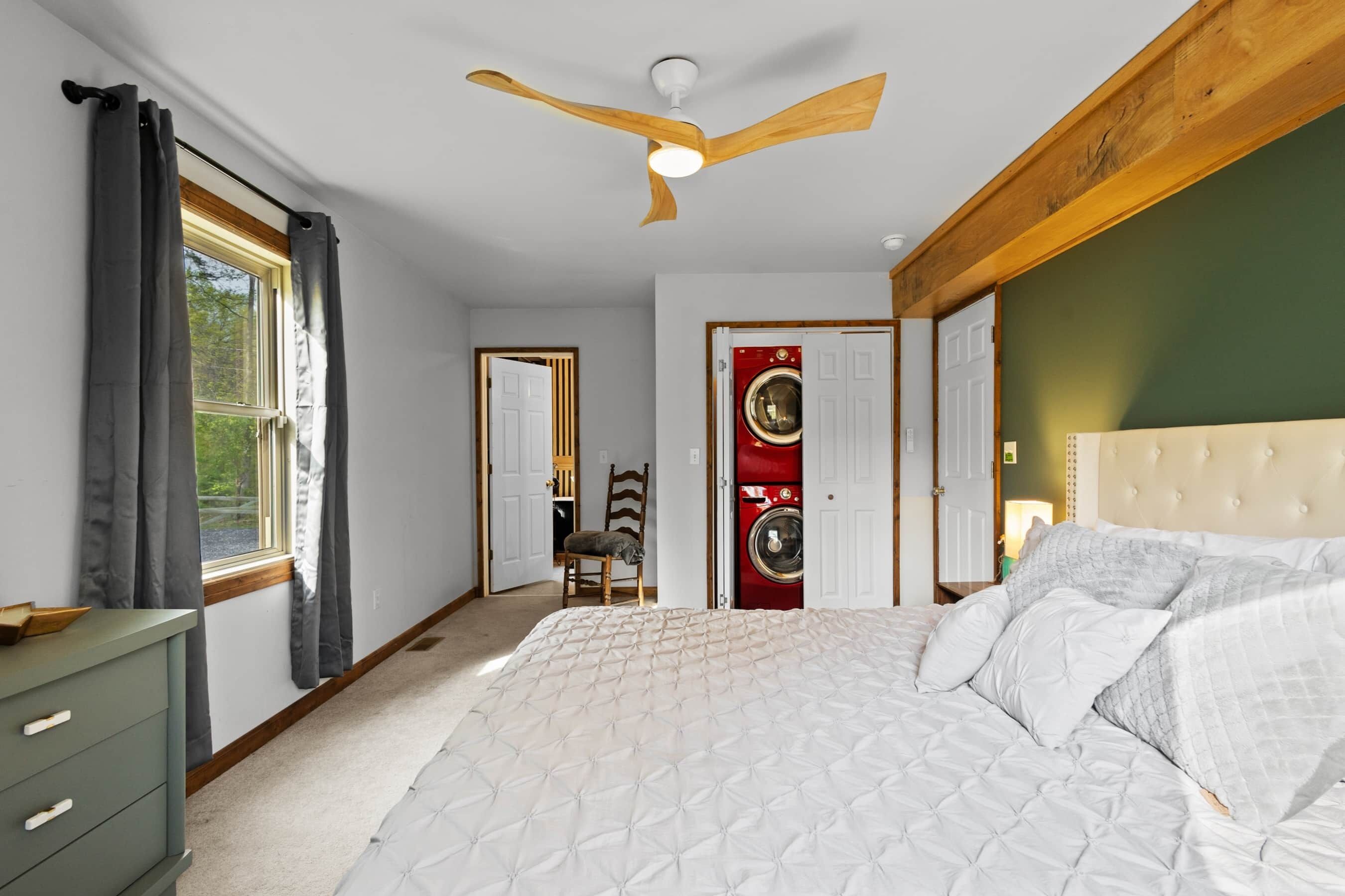A bedroom with a bed, a ceiling fan, a window with curtains, a washing machine, and a dresser.