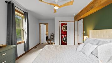 A bedroom with a bed, a ceiling fan, a window with curtains, a washing machine, and a dresser.