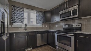 Uma cozinha moderna com armários escuros, eletrodomésticos de aço inoxidável e uma janela com cortinas estampadas.
