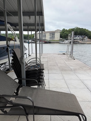 Een overdekt terras met stoelen en tafels, een steiger met boten, en een gebouw op de achtergrond.