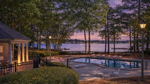 A pool area with lounge chairs, a small building with columns, and a view of a lake at sunset. - Pet Friendly in Great Waters, Docks, Tennis, Pool (Eatonton)
