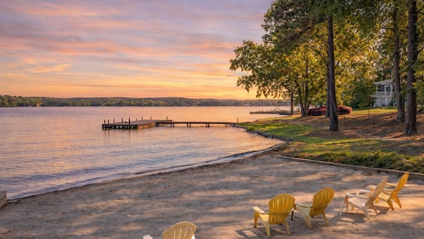 A lakeside view with a wooden dock extending into the water, surrounded by trees and a grassy area with four yellow Adirondack chairs. - Pet Friendly in Great Waters, Docks, Tennis, Pool (Eatonton)