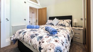 Een slaapkamer met een bed, nachtkastje, lamp, radiator en een deur naar een badkamer.