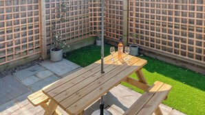 Een houten picknicktafel met bankjes, twee potplanten en twee wijnglazen op een stenen terras.